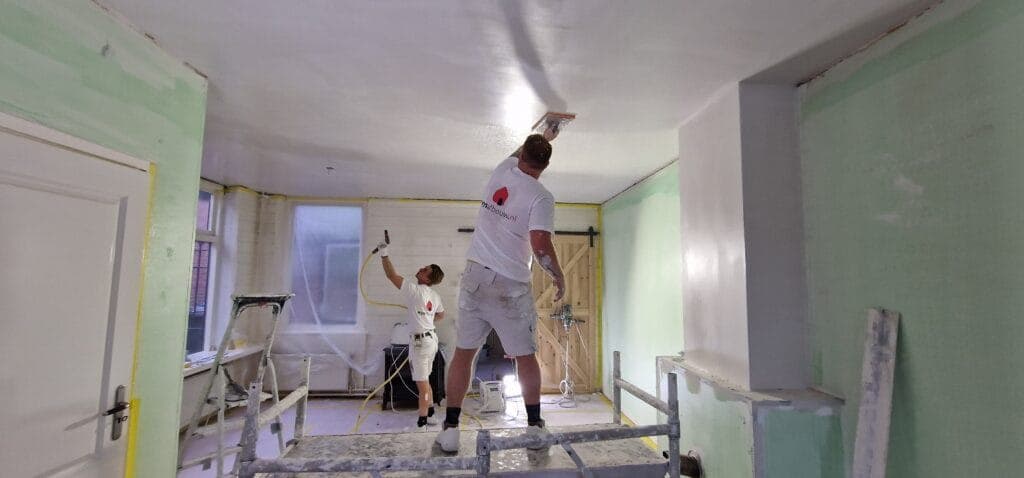 Twee stukadoors werken vanaf een rolsteiger aan een glad plafond
