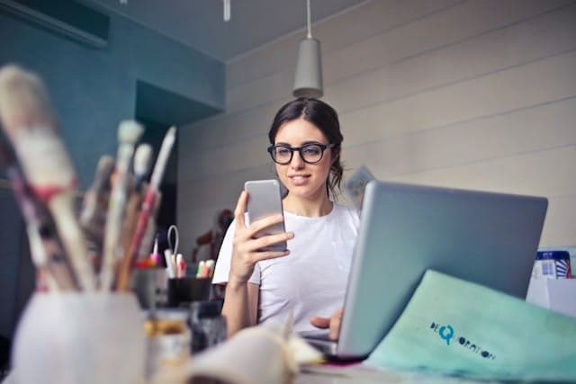 Vrouw met telefoon en laptop, kwasten op de voorgrond